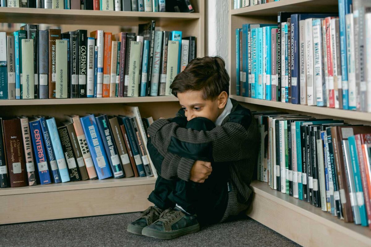 Un niño apoyado en una librería se agarra las rodillas contesto desesperado