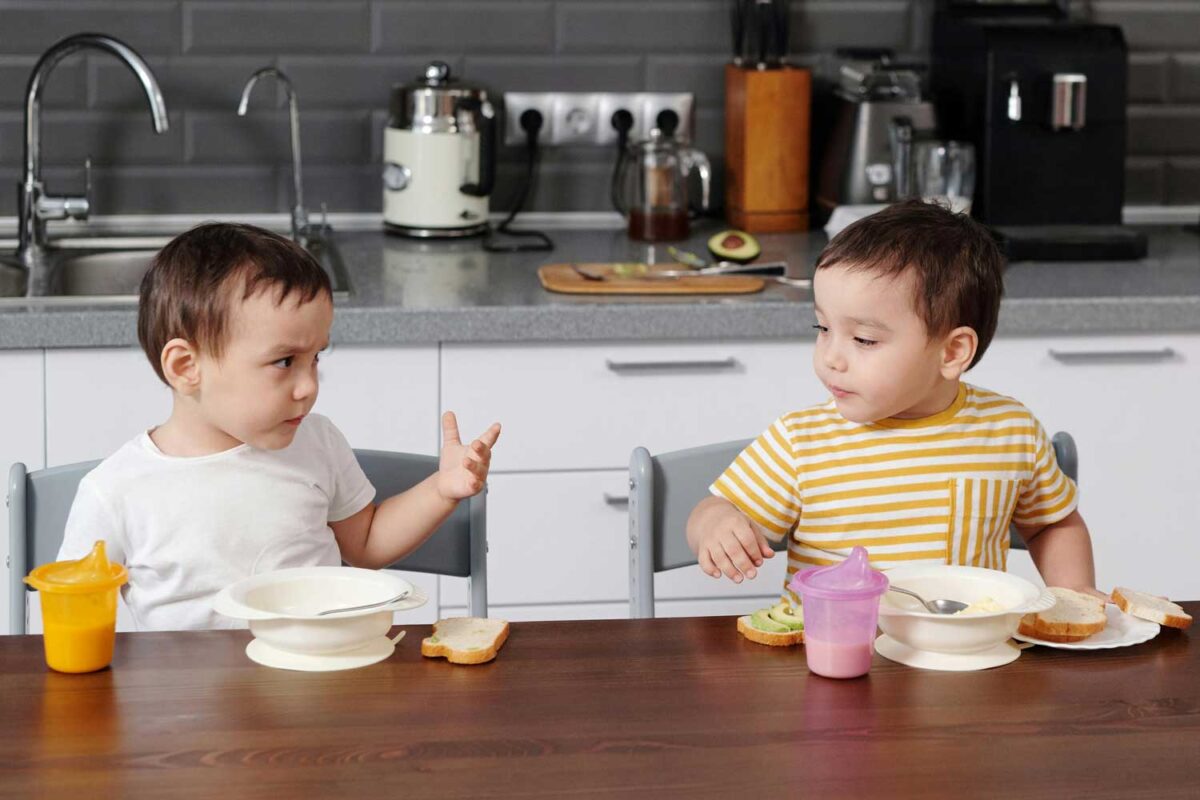 Dos niños de unos 3 años hablan entre ellos mientras comen