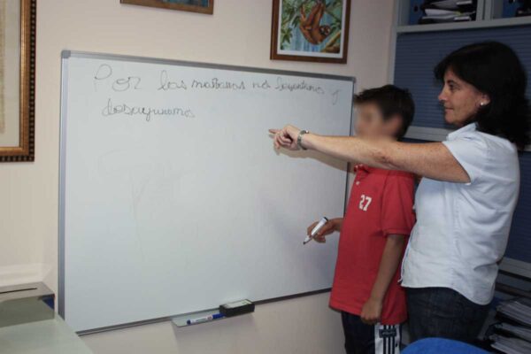 Una terapeuta con un niño delante de la pizarra